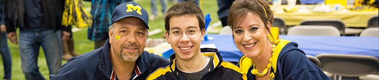 New student posing with parents. All wearing Michigan-themed clothing.